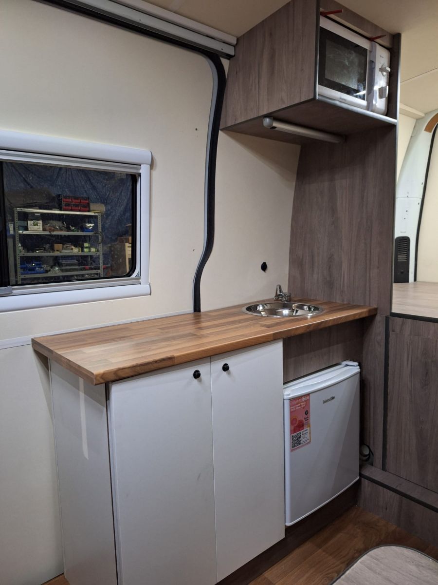 Cuina de la furgoneta camper amb aigüera, nevera, microones i armaris alts