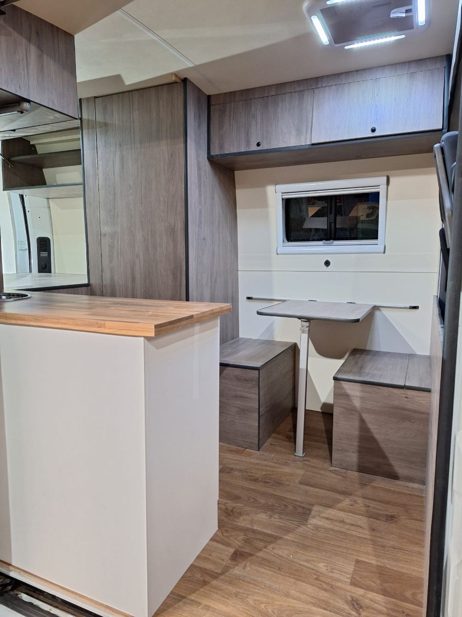 Interior d’una furgoneta camperitzada amb moble de cuina, armari i taula amb seients
